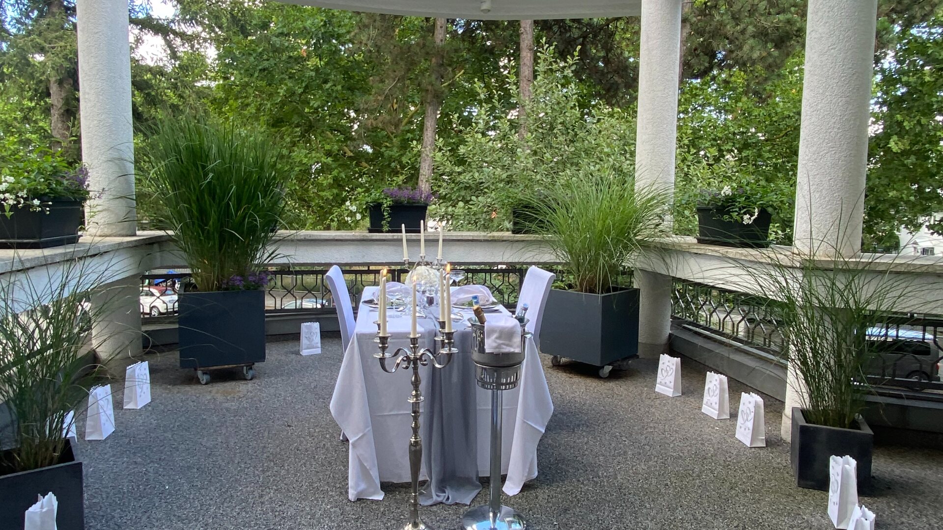 Romantisch eingedeckter Tisch für zwei unter der Pergola der Wirtshaus Alpinia Terrasse, umrahmt von herzförmig aufgestellten Lichtertüten