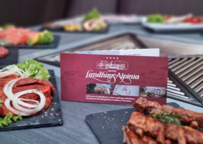 Frisches Fleisch auf Schieferplatte am Grilltisch des Wirtshaus Alpinia, dekoriert mit der Hotelkarte Landhaus Alpinia