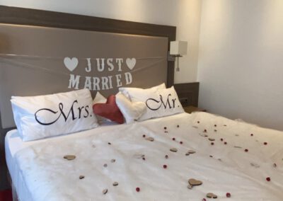 Hotelbett mit Just-Married-Kissen und Rosenblättern zur Hochzeit