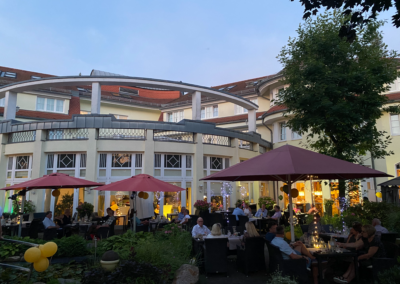 Gäste im Biergarten des Wirtshaus Alpinia in der Abenddämmerung